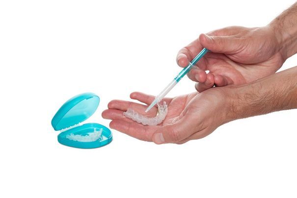 Close-up of two hands holding an at-home tooth whitening tray and bleaching solution