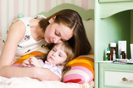 Mother tending to sick daughter in bed next to table full of medications